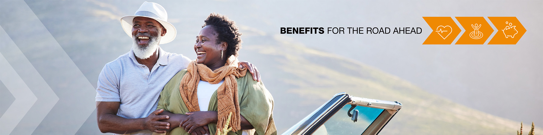 Two smiling people leaning on a convertible with mountains in the background