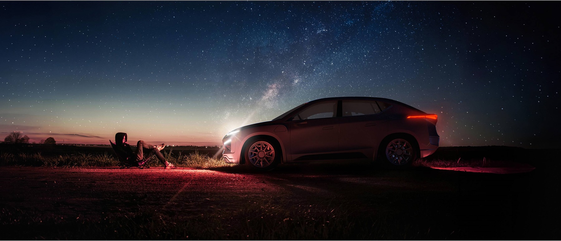 Person sitting in a chair beside a sleek car under a starry night sky