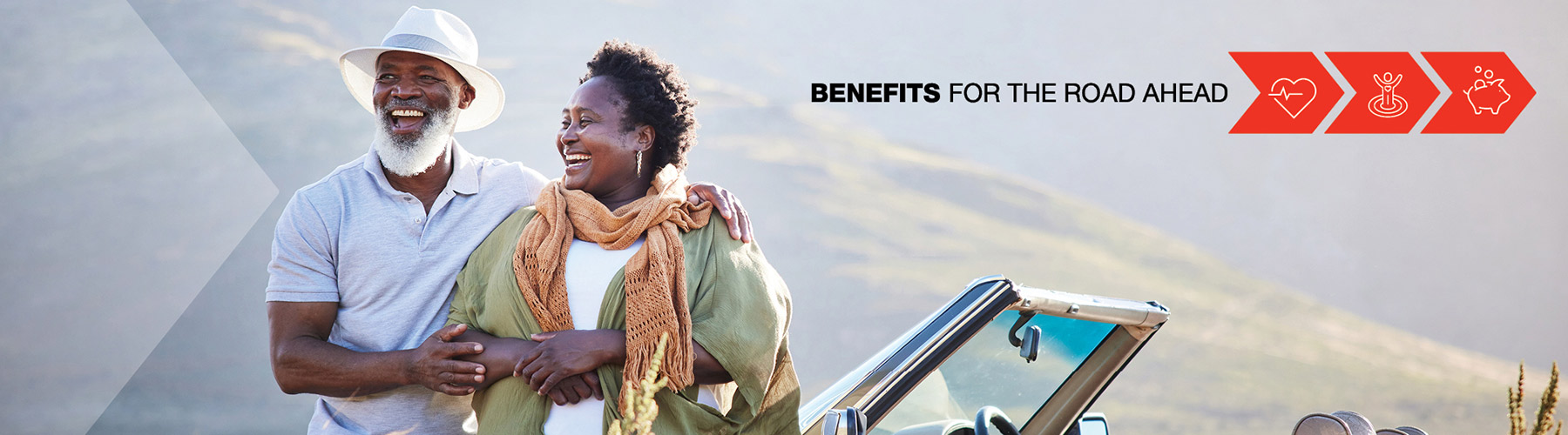 Two smiling people leaning on a convertible with mountains in the background
