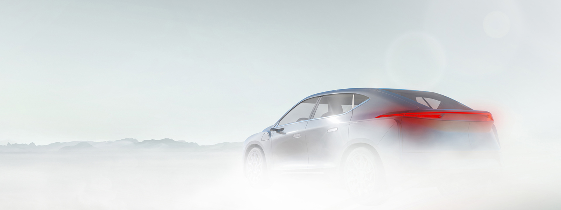 Grey vehicle driving on a foggy road, sky is overcast with mountains in the foreground