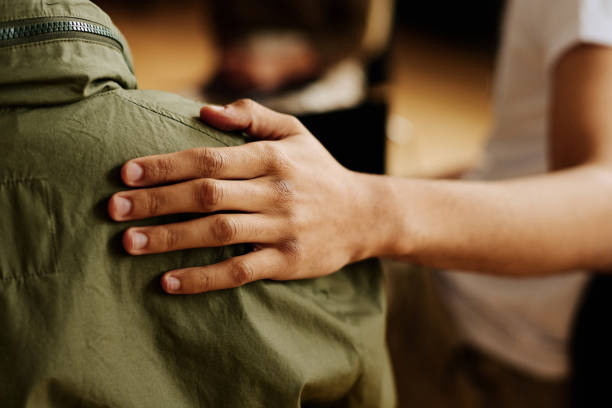 A person sitting and putting their hand on the back of a person wearing a green jacket