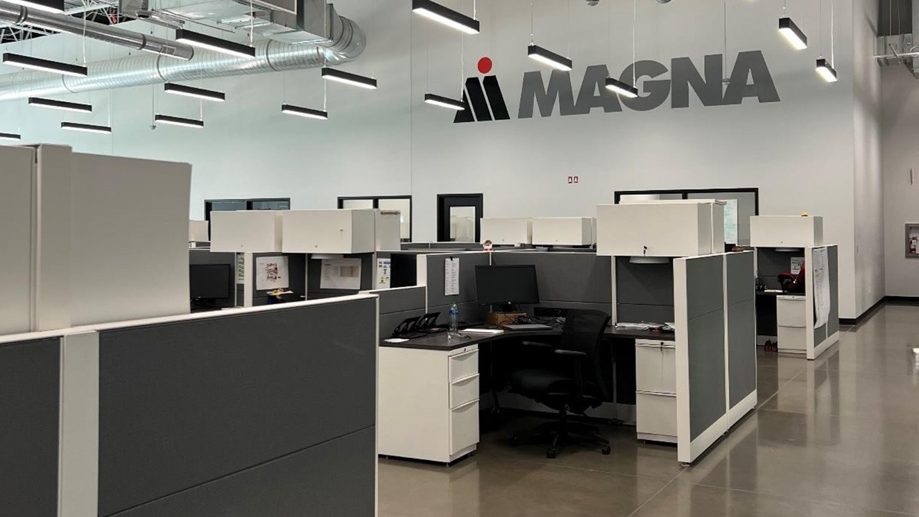 Interior of manufacturing facility office space with cubicles and Magna logo on the wall
