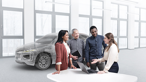 Group of people standing around a table with a lap top with a vehicle in the background