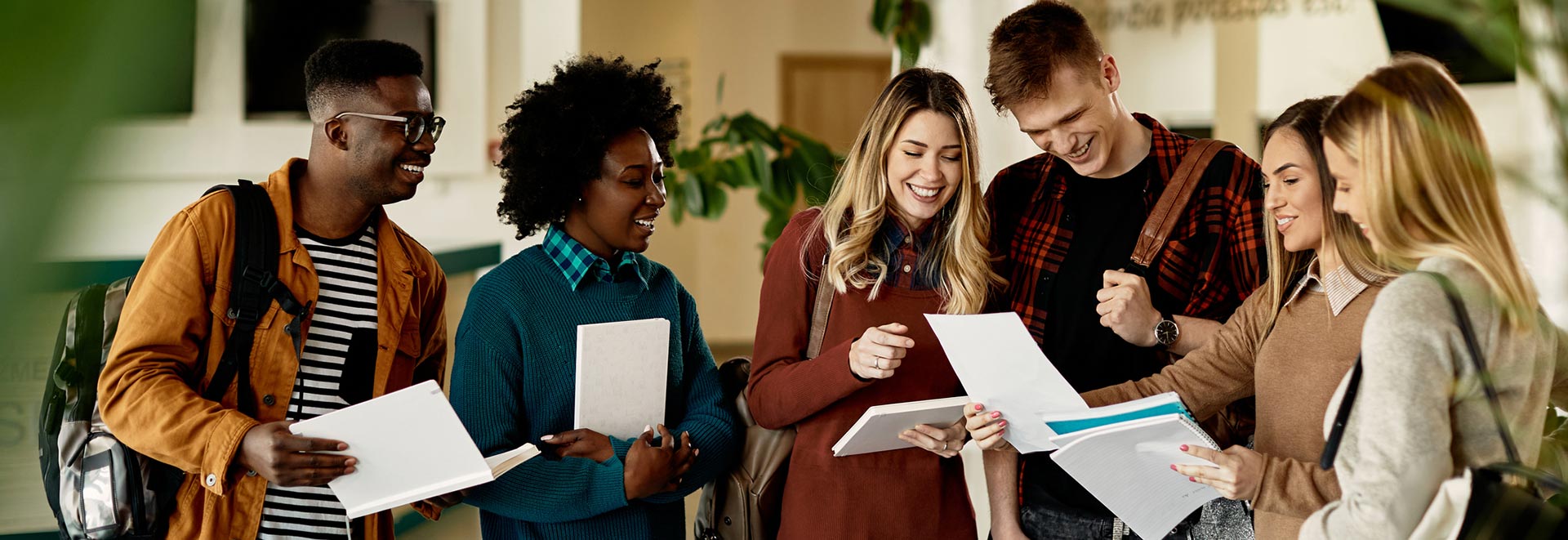 A group of students standing together, looking at papers and smiling