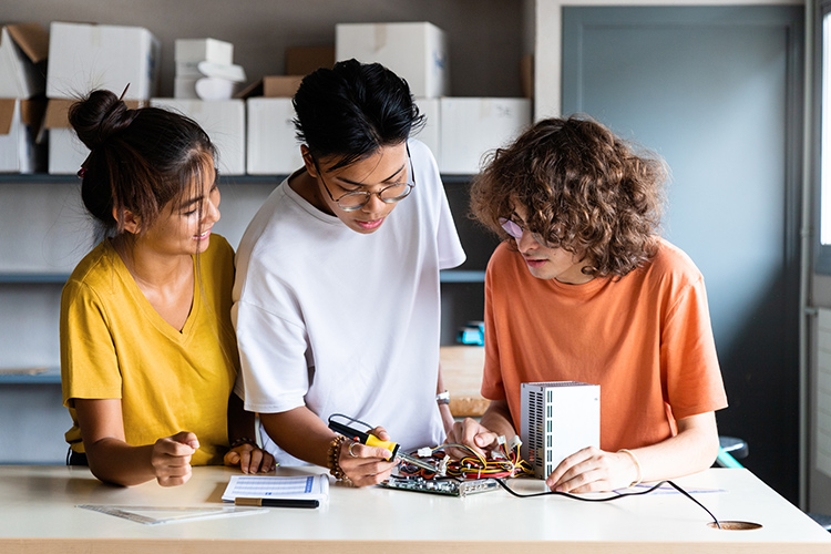 Three students working on a circuit board in a classroom