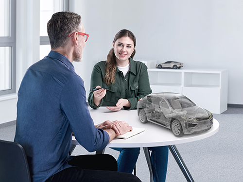 Two people sitting at a table discussing a model of a vehicle
