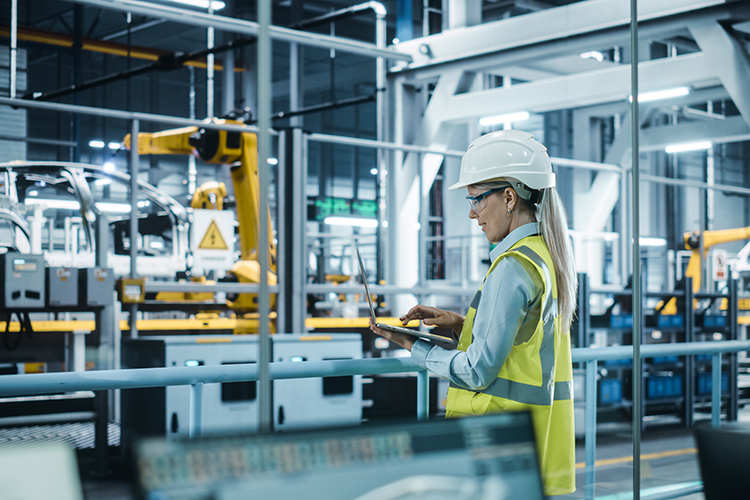 Person on a laptop at a vehicle manufacturing plant watching assembly line