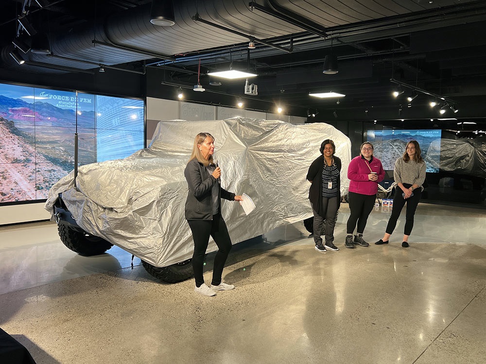 4 people standing in a room with a covered vehicle