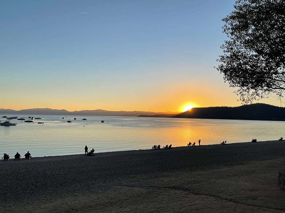 People sitting on the beach with the sun rising in the distance