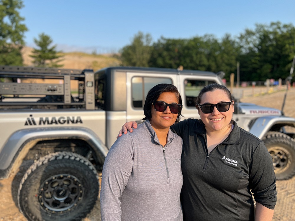 Two people standing outside a Jeep® Gladiator Rubicon on rugged terrain with blue sky and tree in background