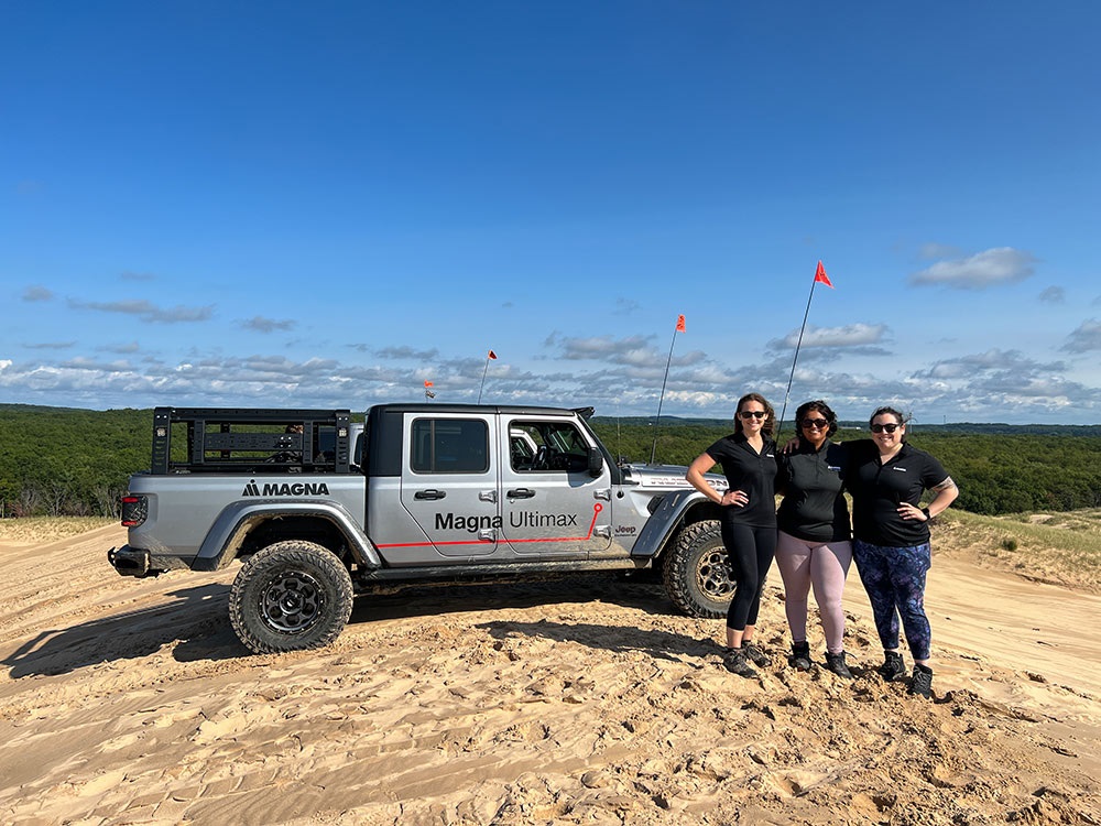 Three people standing outside a Jeep® Gladiator Rubicon on rugged terrain with blue sky and tree in background