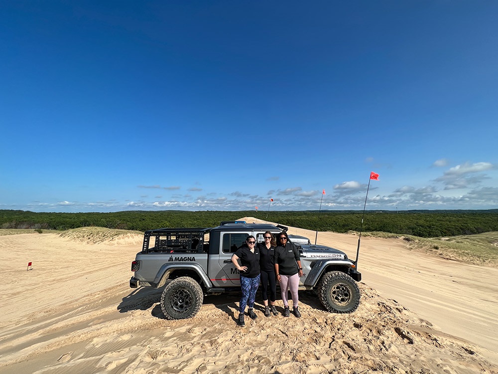 Three people standing outside of a Jeep® Gladiator Rubicon on rugged terrain with blue sky and trees in background