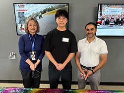 Three people standing together in front of monitors on the wall