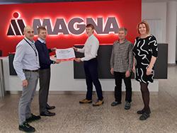 Group of standing together in front of the Magna logo with two people in the middle holding a certificate