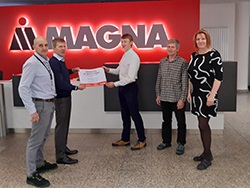 Group of standing together in front of the Magna logo with two people in the middle holding a certificate