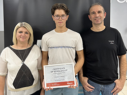 Three people standing together with person in the middle holding a certificate