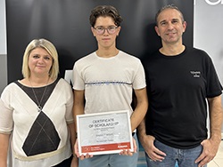 Three people standing together with person in the middle holding a certificate