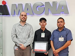 Three people standing in front of the Magna logo with the person in the middle holding a certificate