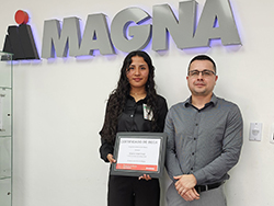 Two people standing in front of the Magna logo with one holding a certificate