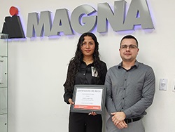 Two people standing in front of the Magna logo with one holding a certificate