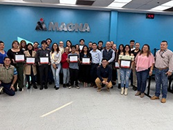 Group of people standing in front of a Magna logo with several people in the front holding certificates