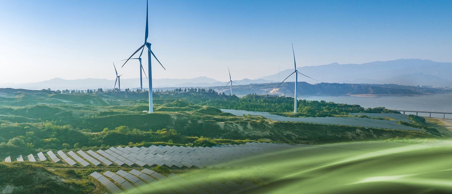 Landschaft mit Windturbinen, Solarmodulen und sanften Hügeln unter klarem Himmel.