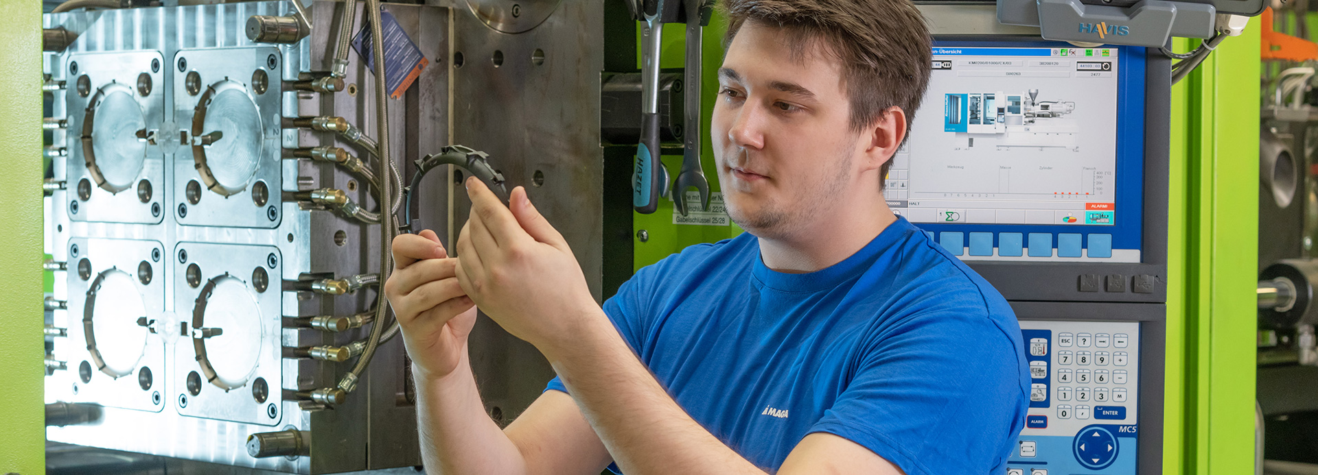 Worker inspecting a molded plastic part beside an injection molding machine