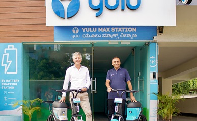 Two people standing in front of a building with electric two-wheelers.