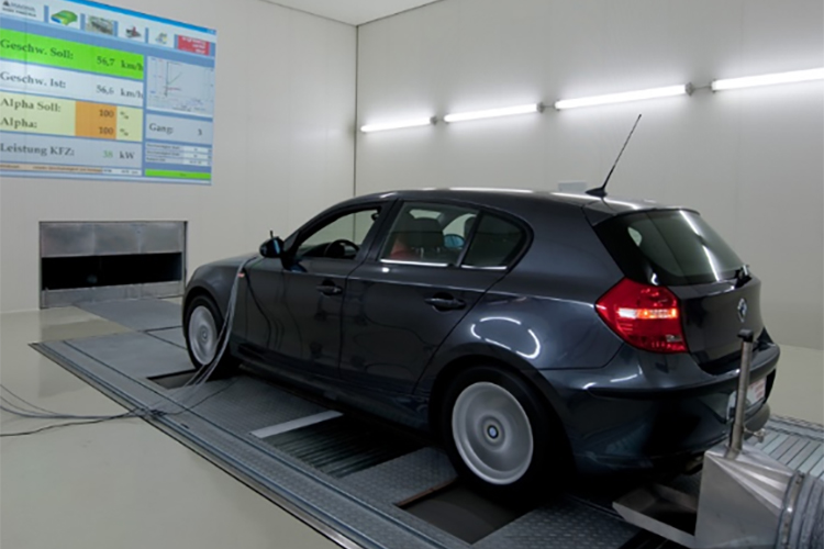 Blue vehicle attached to a 4WD Chassis Dynamometer in a manufacturing facility, data projected onto a wall