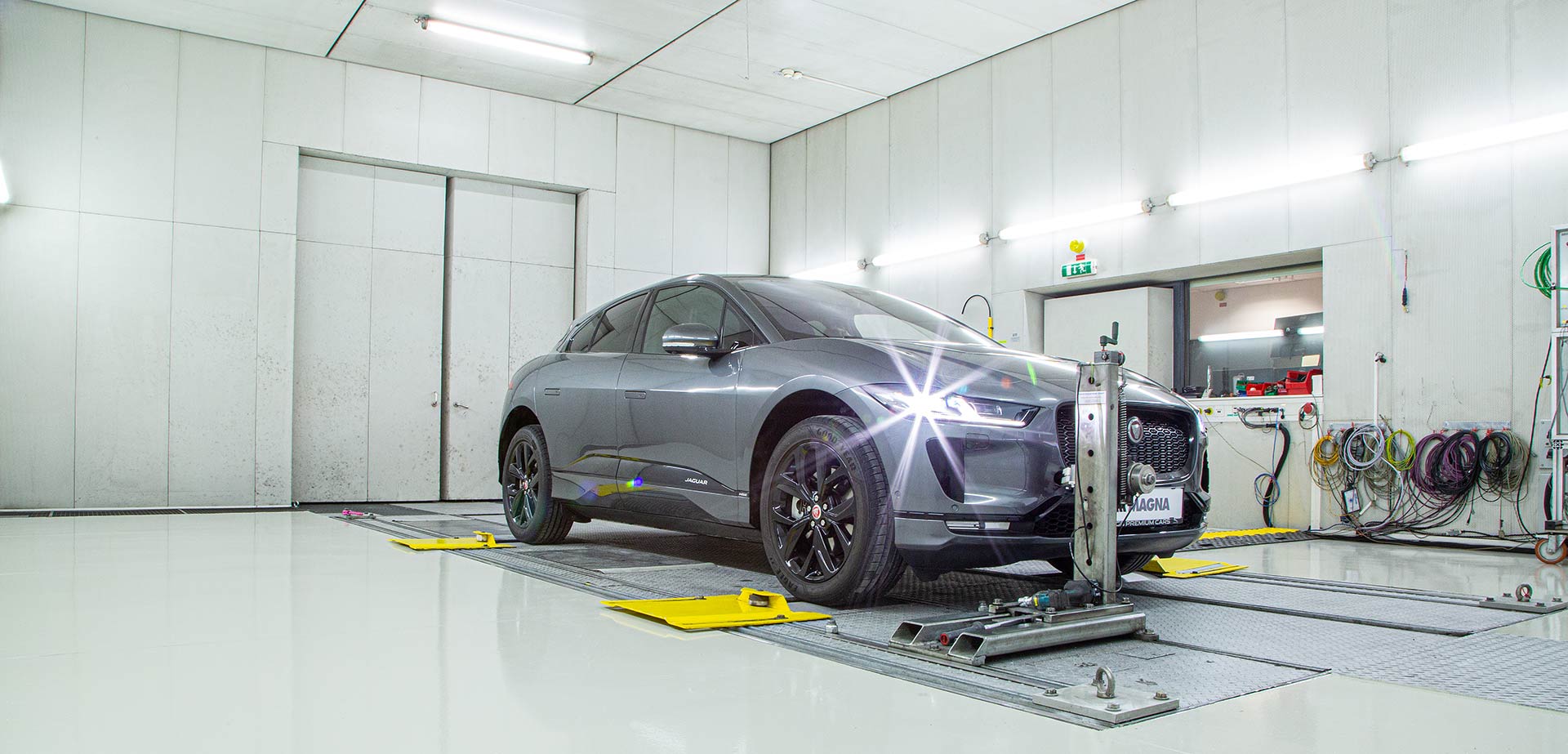 Grey vehicle in a test chamber hooked up to a 4WD Chassis Dynamometer in a manufacturing facility