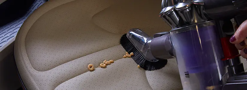 Hand vacuum picking up cereal pieces from a car seat