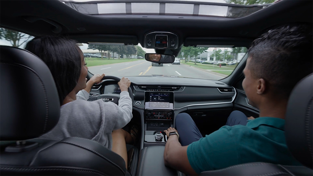 Interior view of a modern car with a sunroof, featuring two people in the front seats. The driver is focused on the road, conveying a calm, relaxed atmosphere.