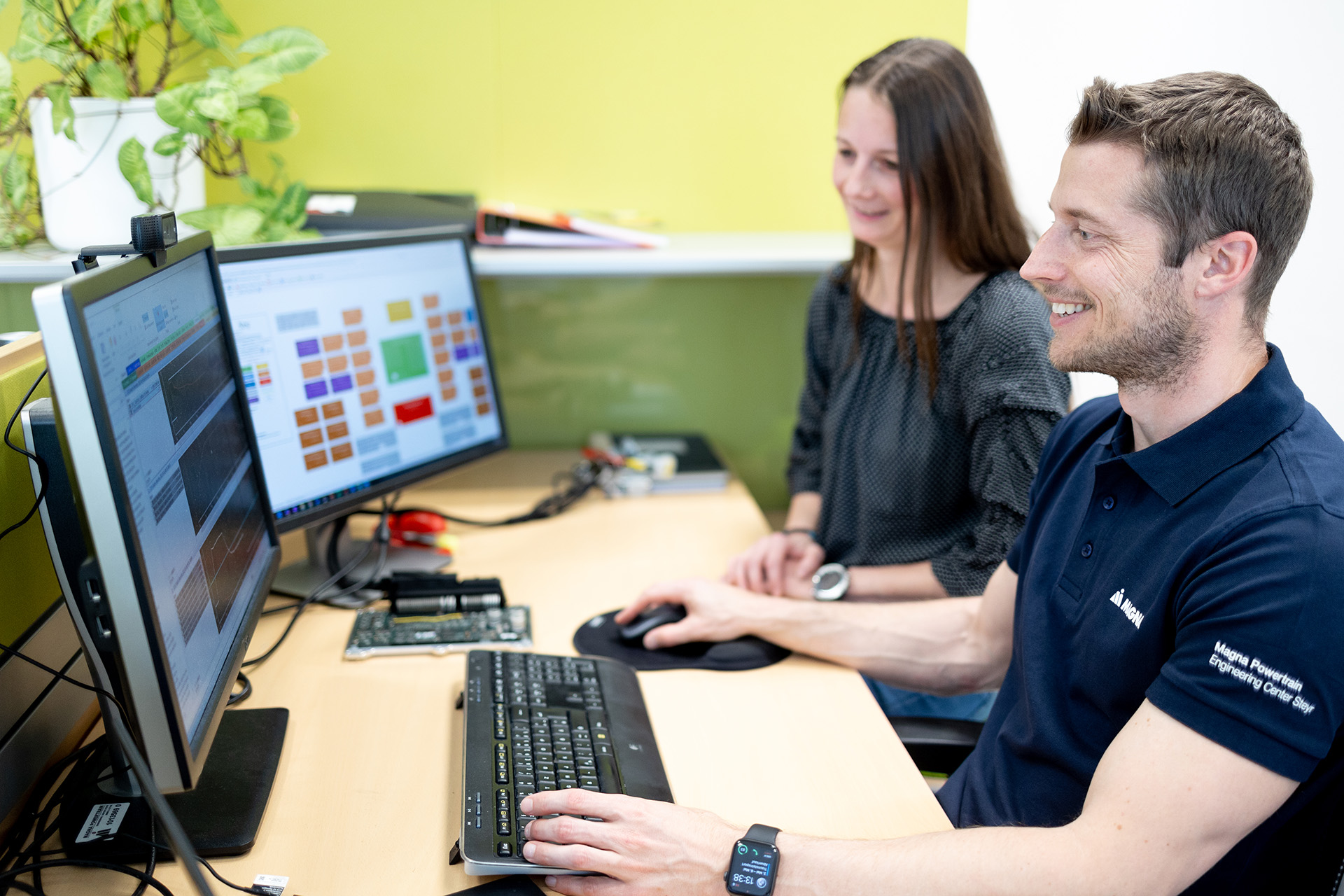 Two colleagues working together at a dual-monitor computer workstation