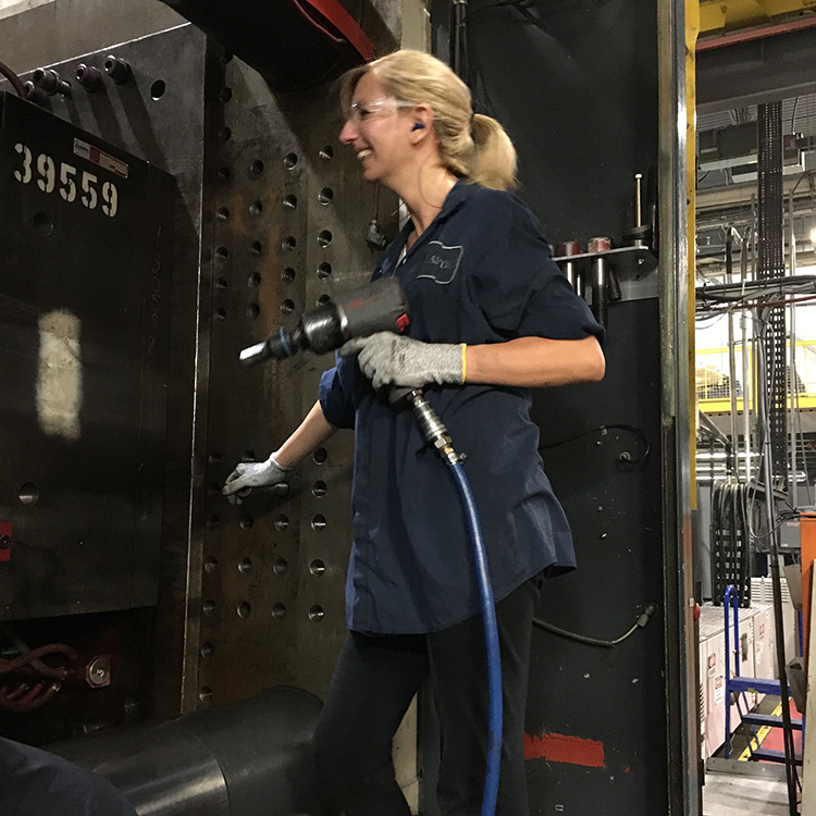Adriana Huntington in a manufacturing facility holding an air gun tightening bolts on an automotive car part.
