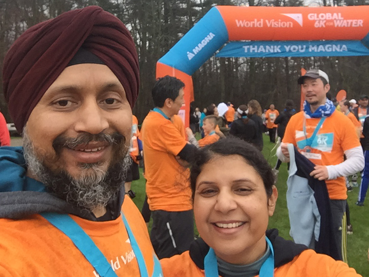 Daljit Banwait and another person standing in front of the finish line for Magna's Global 6K Run for water; other participants in the background
