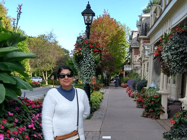 Daljit Banwait wearing sunglasses; standing on a street with shops and beautiful flowers and trees