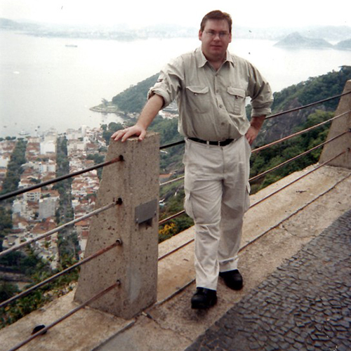 Doug Plester standing on a bridge with houses and the ocean in the background in Brazil