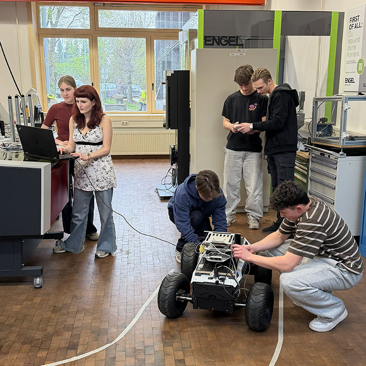 Five students in a workshop engage in programming and coding a remote controlled vehicle, creating an atmosphere of collaboration and focus.