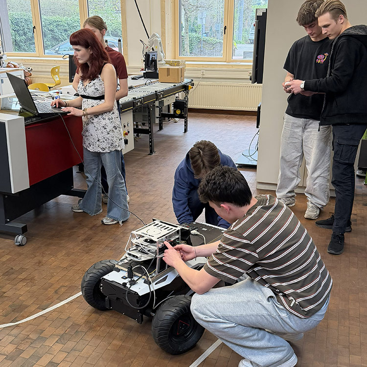 Five students in a workshop engage in programming and coding a remote controlled vehicle, creating an atmosphere of collaboration and focus.