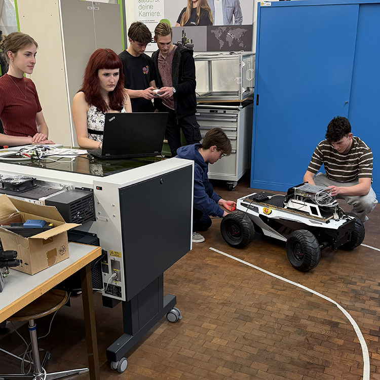 Five students in a workshop engage in programming and coding a remote controlled vehicle, creating an atmosphere of collaboration and focus.