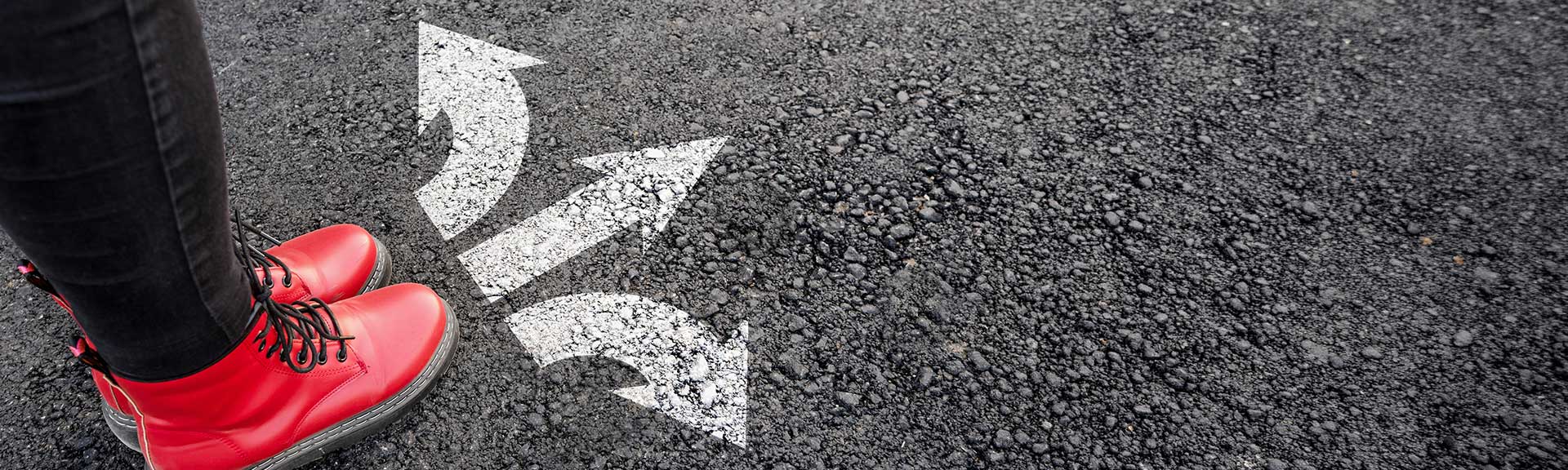 Red boots standing on a paved road with white direction arrows pointing left, right and forward