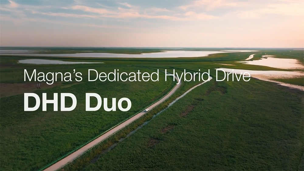 Overhead view of a vehicle driving along a tree lined road with the sun setting and lakes in the foreground