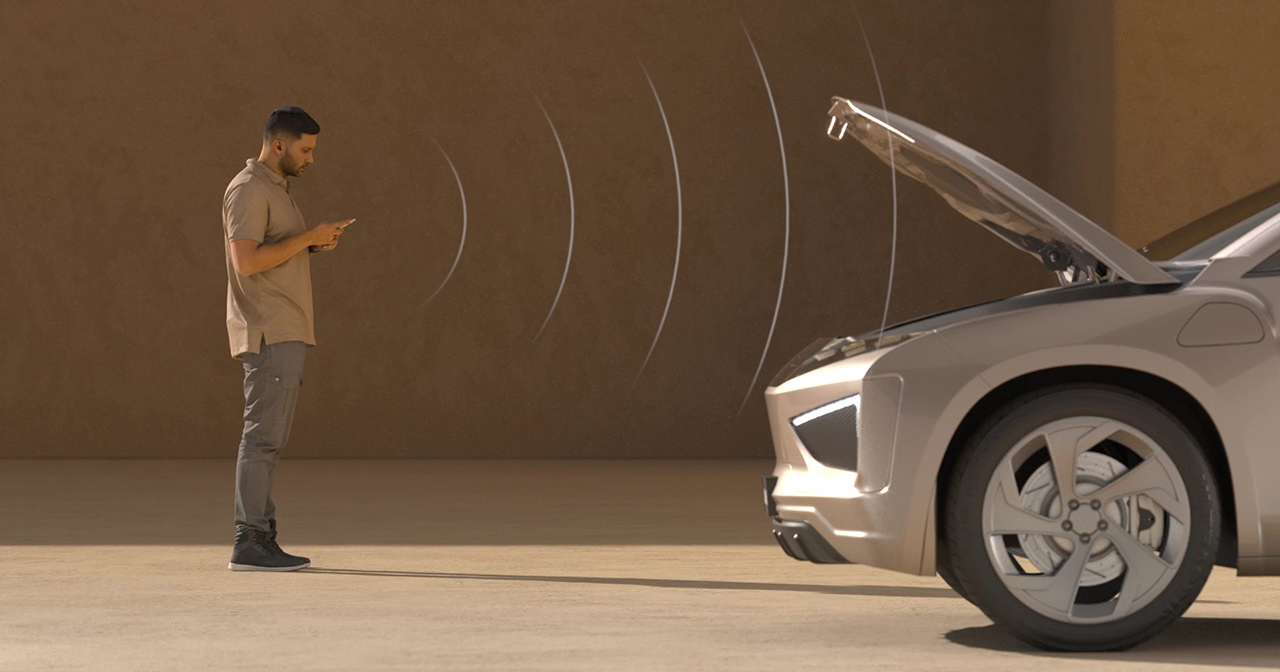 Person standing in front of a grey vehicle using a smart phone to open the frunk remotely.