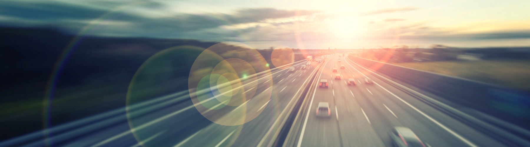 Cars driving along a highway with the sun setting in the distance