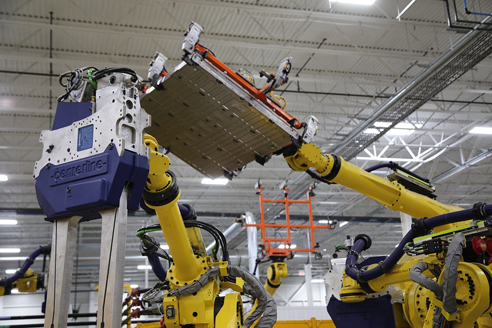EV Battery Enclosure being lifted by robots in a manufacturing facility.