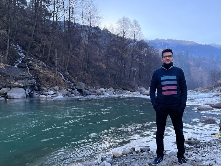 Nischay Hiremath standing on the banks of a river with mountains in the background