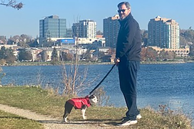 Darren Charbonneau walking his dog by the shores of a lake with buildings in the background