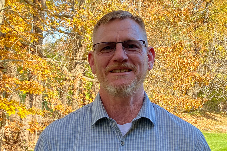 Kevin Kammerer standing in front of trees that are turning colour in the fall.