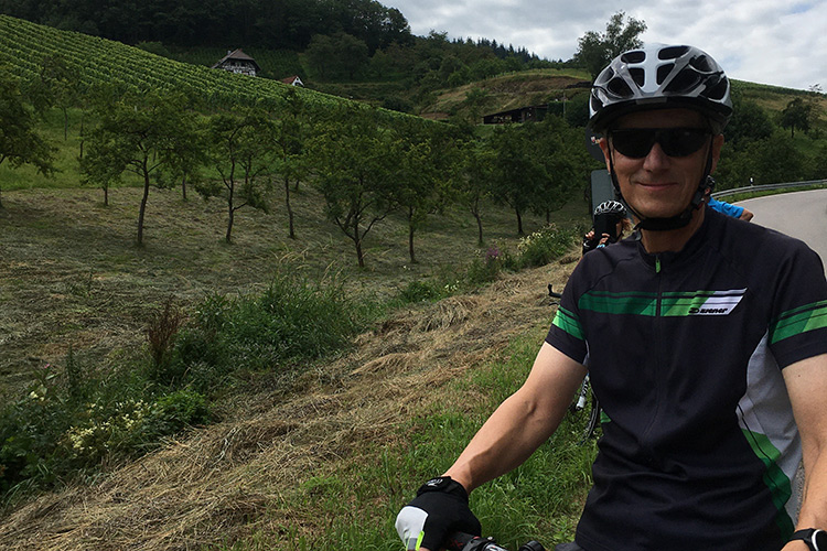 Volker Ludwig riding his bike along a road with a mountains and fields in the background