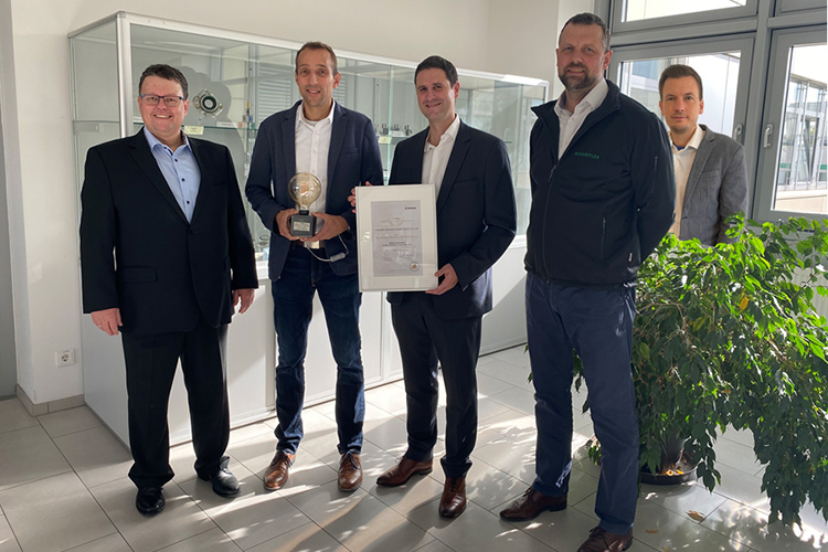 Group of people standing in a lobby with a certificate and trophy